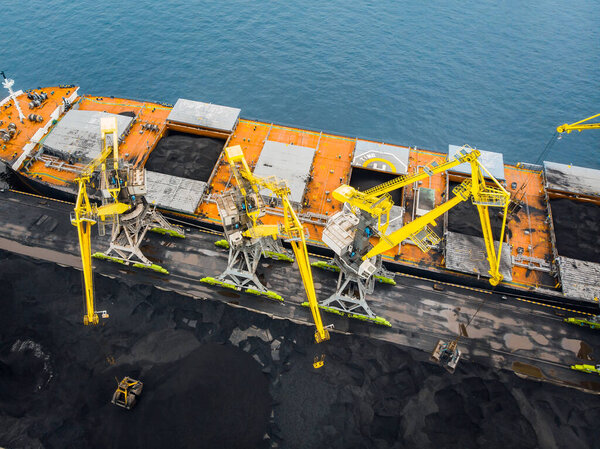 Погрузка угольного антрацита в порт на грузовом танкере с крановым ведром поезда. Вид сверху с воздуха