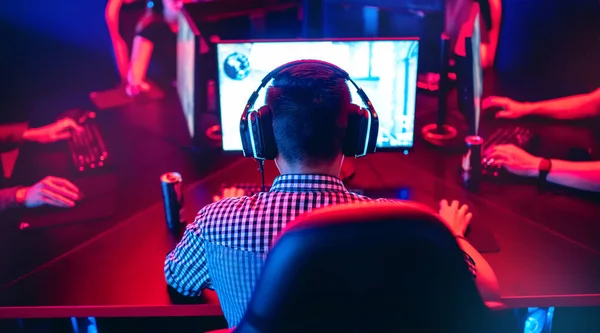 Jugador profesional jugando torneos de juegos en línea ordenador PC con auriculares, fondo rojo y azul borrosa —  Fotos de Stock