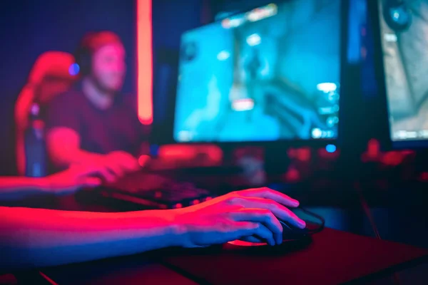 Jugador profesional jugando torneos de juegos en línea ordenador PC con auriculares, fondo rojo y azul borrosa — Foto de Stock