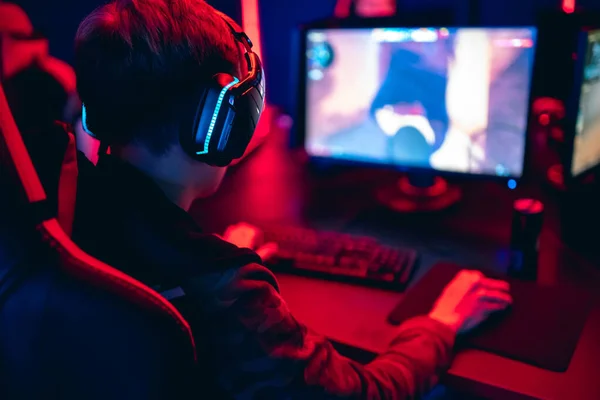 Jugador profesional jugando torneos de juegos en línea ordenador PC con auriculares, fondo rojo y azul borrosa —  Fotos de Stock