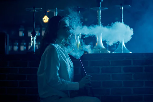 Jovem mulher bonita no clube noturno fumar narguilé ou shisha bar, fundo azul — Fotografia de Stock