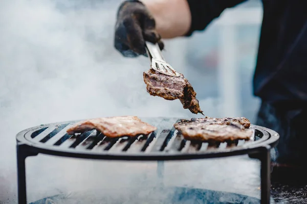 Vařit grily steaky a vepřové žebírka zahájit oheň. Obrátí maso s kleštěmi. Koncept pouličního jídla — Stock fotografie