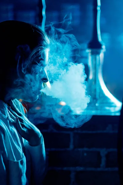 Красивая женщина в ночном клубе курить кальян или шиша бар, синий фон — стоковое фото