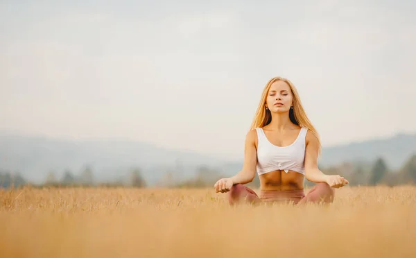 Young girl in sportswear with closed eyes, lotus position practices yoga in field. Freedom concept — Stock Photo, Image