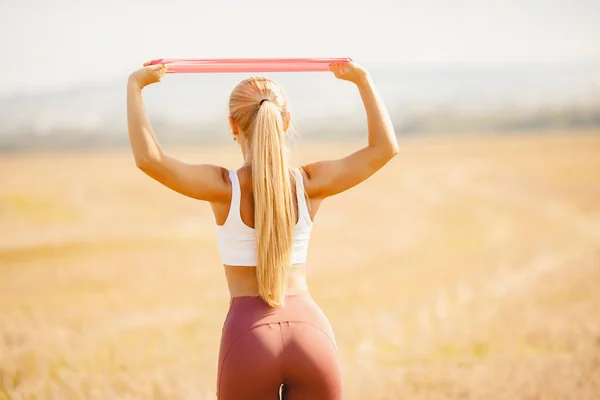 Linda menina atleta loira realiza exercícios ao ar livre no parque fitness alongamento elásticos — Fotografia de Stock