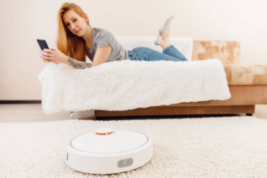 Genç kız halı üzerinde çalışan otomatik akıllı robot süpürge kullanıyor.