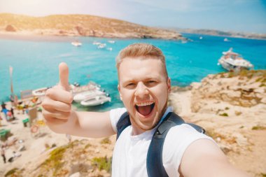 Male tourist sunglasses taking selfie photo on beach Blue Lagoon Comino Malta water mediterranean sea clipart