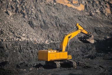 Bir kova dolusu siyah kömürü olan büyük sarı kazıcı açık madende yükleme yapacak.
