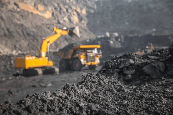 Sert siyah kömüre odaklan, endüstriyel taş ocağı benimkini aç. Arka plandaki bulanık mineral antrasit kazıcısını büyük sarı kamyona yükle — Stok fotoğraf