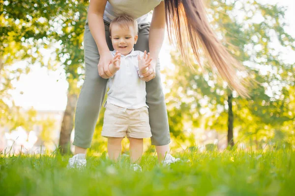 Feliz sorrindo criança menino faz primeiro passo no parque, mamãe ajuda — Fotografia de Stock