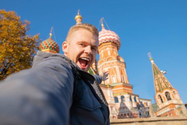 Male tourist makes selfie photo on background Saint Basil Cathedral Red Square in Moscow, Russia autumn clipart