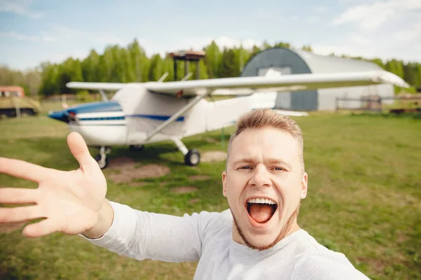 Пілотний чоловік робить селфі фото на фоні літака, щасливо посміхаючись — стокове фото