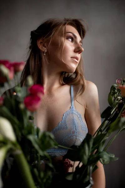 Красива молода жінка в мереживо-блакитній білизні тримає трояндові квіти, концепція догляду за шкірою — стокове фото