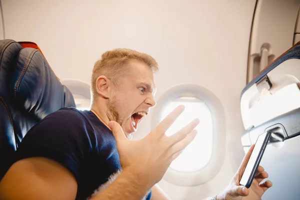 De man schreeuwt en neemt het mobieltje aan boord van het vliegtuig kwalijk. Concept fobie en gebrek aan internetverslaving — Stockfoto