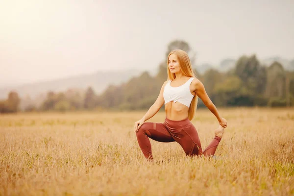 Hermosa chica con el pelo largo y rubio en ropa deportiva se extiende en el campo del parque de la salida del sol. Concepto de Yoga de Beneficios para la Salud —  Fotos de Stock