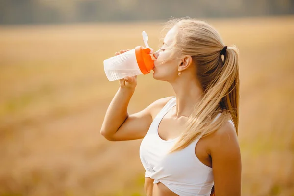 Beautiful blonde drinks water after workout in park from sports bottle — Stock Photo, Image