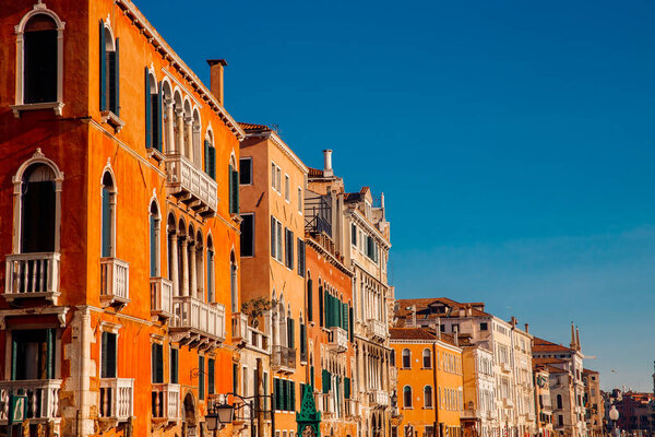 Clear warm day, sun plays colors of orange brick typical European houses with arches on Windows and small balconies against blue sky