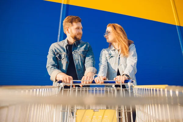Junges Paar hält Einkaufswagen für Lebensmittel in der Hand und steuert auf Ladeneingang zu — Stockfoto