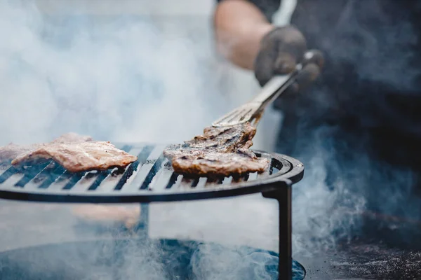 Izgara biftek ve domuz pirzolası. Maşayla eti çevirir. Sokak yemekleri konsepti — Stok fotoğraf