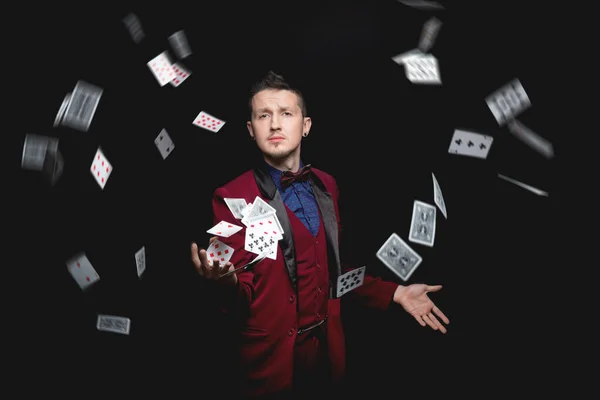 Ілюзіоніст чарівник показує магію з гральними картками на чорному тлі — стокове фото