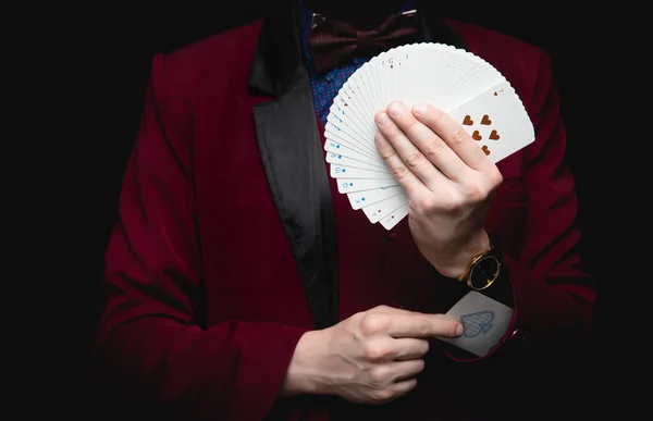 Illusionist man shows fan of playing cards takes ace out hand on black background