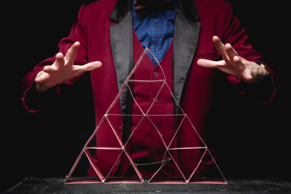 Magician shows trick pyramid with playing cards on dark background — Stock Photo, Image