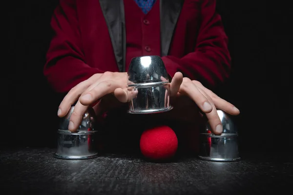 Magician shows shell game of thimbles with circles and ball, black background. Concept deception, sleight hand — Stock Photo, Image