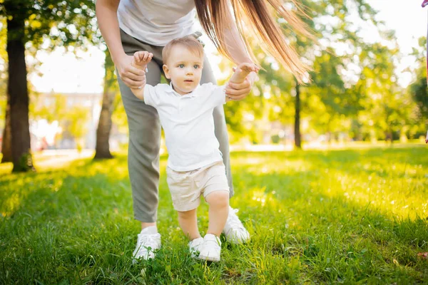 Criança bebê dá o primeiro passo com a ajuda da mãe no parque. Conceito pais ensinam a andar — Fotografia de Stock