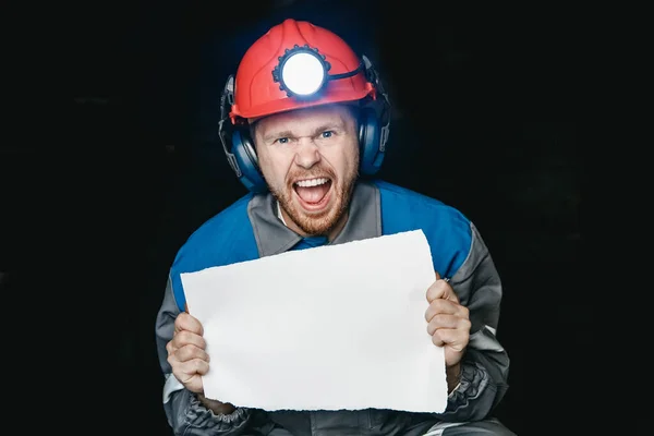Homem raivoso mineiro grita e franze a testa, segura folha de papel para texto. Concept levantamento greve de mineração — Fotografia de Stock