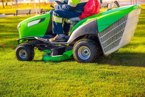 Gardener worker on lawn mower tractor cuts green grass