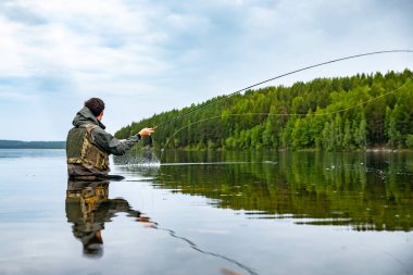 Fisherman using rod fly fishing in river morning standing in water clipart