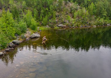 Balıkçı oltayı dağ nehrine botlarıyla fırlattı. Balıkçı somonu, sabah. Havadan üst görünüm