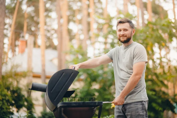 Человек жарит мясо на гриле барбекю в саду — стоковое фото