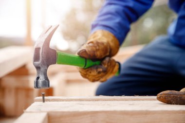 Male builder in yellow gloves hammer nail into wooden structure. Construction concept