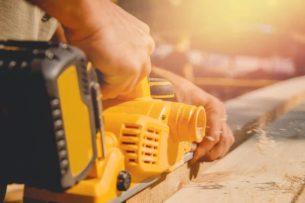 Αρσενικό χέρι εργαζόμενος κρατήσει ηλεκτρικό έργο planer με ξύλινη σανίδα, λεία σκόνη — Φωτογραφία Αρχείου