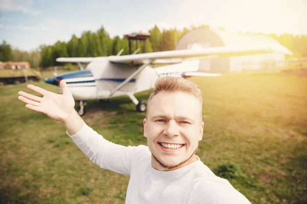 Gelukkige mannelijke piloot selfie foto aviator glimlachend op de achtergrond propeller aangedreven vliegtuigen. Reisverhuur concept — Stockfoto