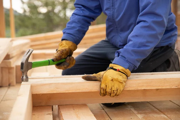 Constructor masculino en guantes amarillos clavo de martillo en la estructura de madera. Concepto de construcción — Foto de Stock