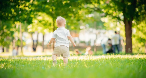 Menino de volta em shorts e camisa branca deixar parque na grama verde. Espaço de cópia — Fotografia de Stock