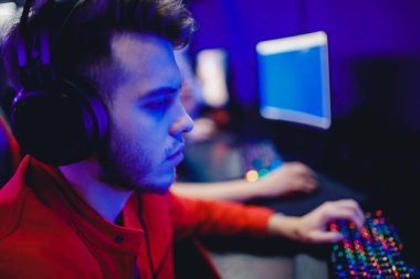 Genç oyuncu internet kulübü kafesinde kulaklıkla video oyunu oynuyor, mavi renkte. Esports konsepti