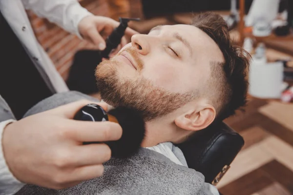 Barber traite la peau masculine avec de la poudre de talc et de la lotion pour les blessures et l'irritation après le rasage de la barbe avec un rasoir — Photo