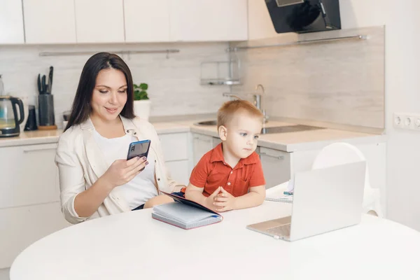 Kobieta na urlopie macierzyńskim pracuje w domu online z laptopem w kuchni z małym dzieckiem. Concept mama praca podczas kwarantanny izolacji podczas Covid-19 — Zdjęcie stockowe