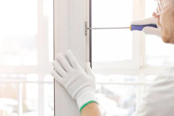 Worker man installs plastic windows white lock and seal adjustment