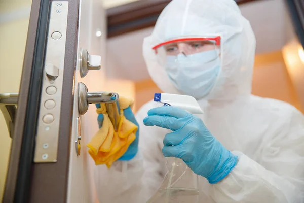 Απολύμανση και καθαρισμός χειρολαβών πόρτας του σπιτιού από μόλυνση με ιό και μικρόβια σε βιοχημική στολή. Έννοια προστασίας από τον ιό Coronavirus — Φωτογραφία Αρχείου