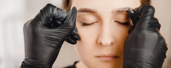 Master applies thread to woman on brow. Correction and tinting eyebrows — Stock Photo, Image