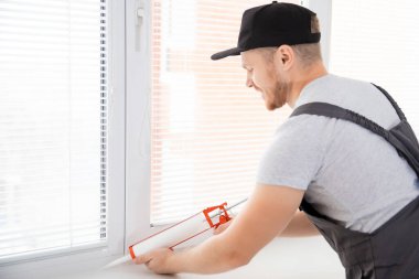 İnşaat işçisi evde pencere onarımı ve montajı için silikon tüp kullanıyor