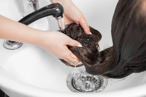 Shampooing Haare im Wellness-Schönheitssalon, Friseur wäscht Schaum aus dem Kopf der jungen brünetten Frau — Stockfoto