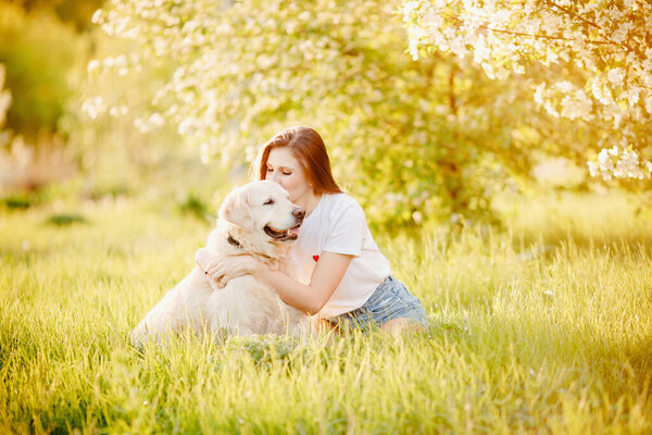 Young woman owner hugs dog Labrador Retriever outdoors in green grass park, summer day