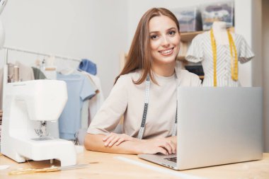 Gülümseyen kadın terzi dizüstü bilgisayarda çalışıyor, dikiş siparişleri alıyor. İş aşkı kavramı
