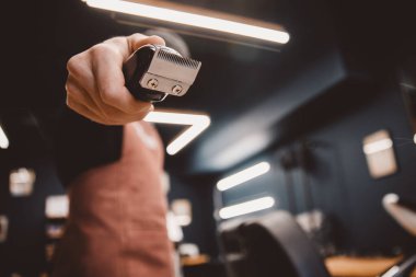 Berberin elinde saç makasıyla arka planda berber dükkanı var.