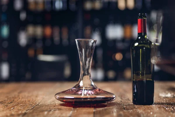 Vinho tinto em garrafa e decantador fica em mesa de madeira no restaurante, fundo escuro — Fotografia de Stock